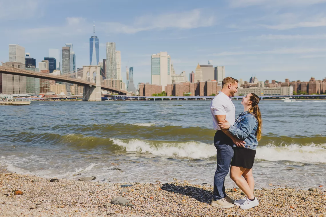 Couple holding each other near the beach with the nyc skyline behind them