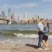 Couple holding each other near the beach with the nyc skyline behind them