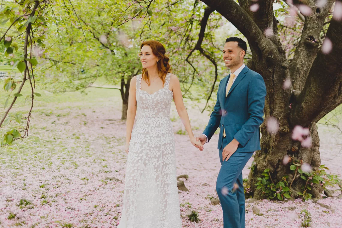 Couple holding hands underneath a cherry blossom tree walking.