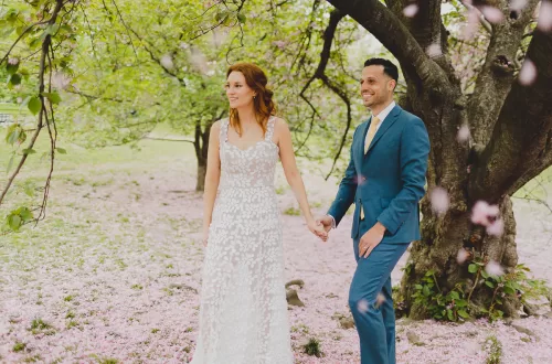 Couple holding hands underneath a cherry blossom tree walking.