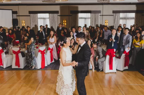 Asian Couple dancing together on the dance floor with guests behind them cheering them on.