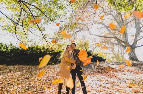 Interracial couple throw autumn leaves in the air in Fort Greene Park