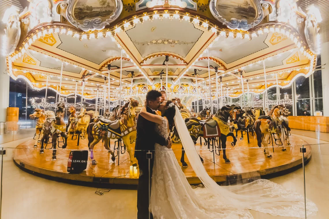 Asian couple in front of horse carousel kissing