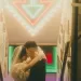 Couple hugging each other in a stairwell with a neon sign arrow pointing at them